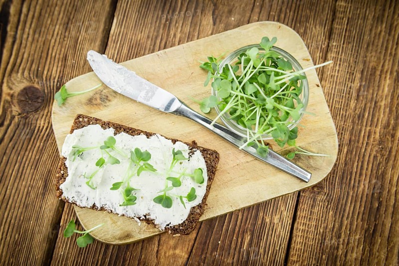 Slice of wholemeal bread with fresh cutted cress and cream cheese on an old wooden table (selective focus, close-up shot)