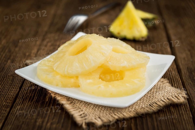Preserved Pineapple Rings as high detailed close-up shot on a vintage wooden table, selective focus