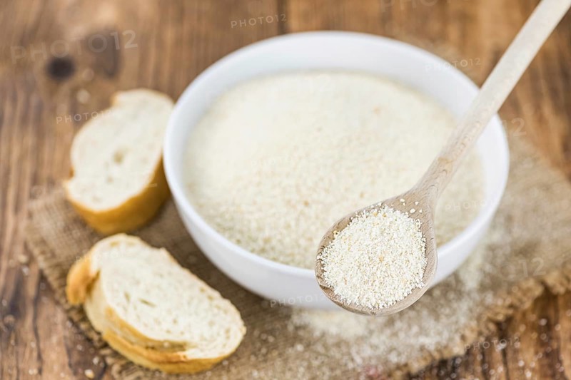 Wooden spoon with Breadcrumbs (close-up shot, selective focus) on an old wooden table