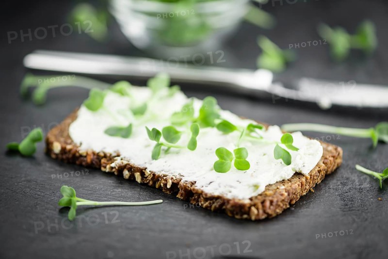 Slate slab with cream cheese and fresh cress on a slice of wholemeal bread (close-up shot, selective focus)