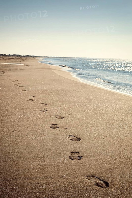 Coastal landscape with thin beach and blue sea, footsteps in sand