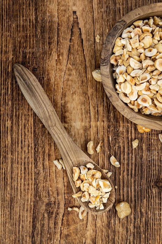 Portion of freshly chopped Hazelnuts on an old wooden table as detailed close up shot (selective focus)