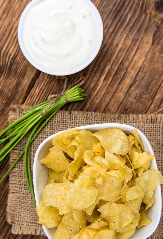 Potato Chips (Sour Cream taste) on rustic wooden background (close-up shot)
