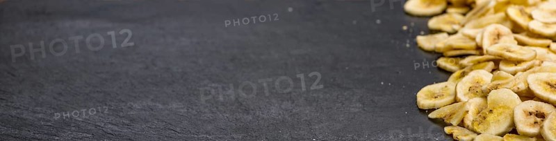Some Dried Banana Chips on a slate slab as detailed close-up shot, selective focus