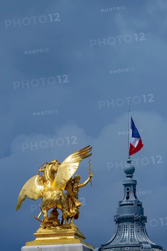 Column with the group of figures Fama of Agriculture on the Pont Alexandre III bridge over the Seine, behind it the dome of the Grand Palais with the French national flag, Tricoloe, Paris, ÃŽle-de-France, France, Europe