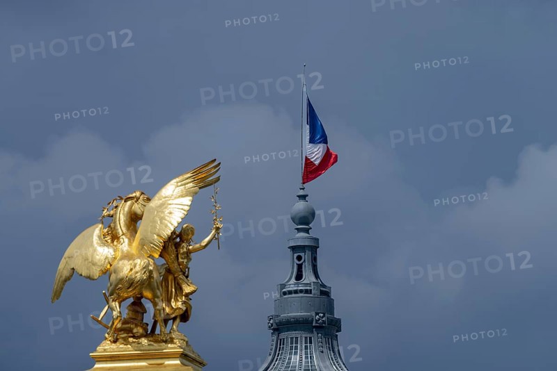 Column with the group of figures Fama of Agriculture on the Pont Alexandre III bridge over the Seine, behind it the dome of the Grand Palais with the French national flag, Tricoloe, Paris, ÃŽle-de-France, France, Europe