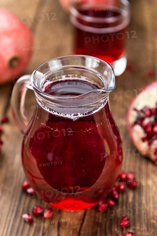 Pomegranate juice as high detailed close-up shot on a vintage wooden table (selective focus)