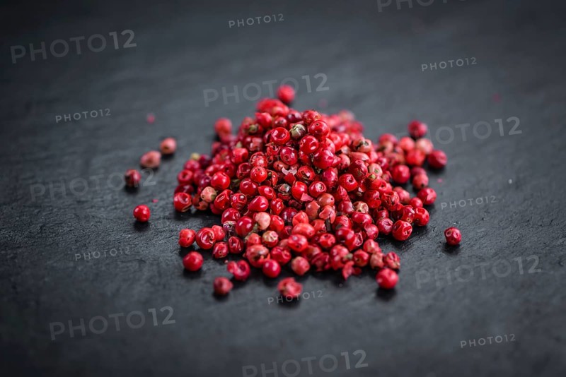 Portion of Pink Peppercorns as detailed close up shot on a slate slab, selective focus