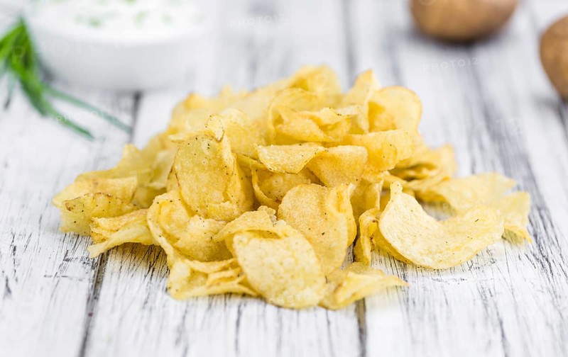 Potato Chips (Sour Cream taste) on rustic wooden background (close-up shot)