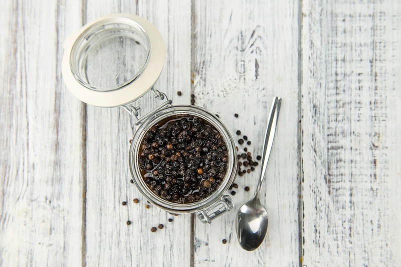 Wooden table with preserved black Peppercorns, selective focus, close-up shot