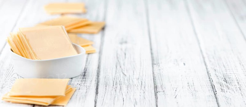 Cheese (sliced) on an old wooden table as detailed close-up shot (selective focus)