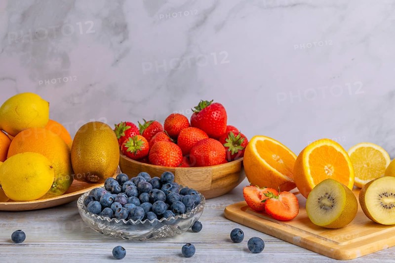 Harmonious still life of various fruits, strawberries, lemons, oranges, kiwis and blueberries, partly sliced