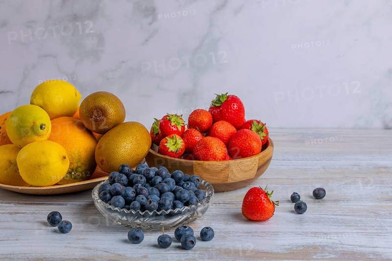 Harmonious still life of various fruits, strawberries, lemons, oranges, kiwis and blueberries on wood against a marble background