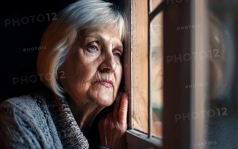 An elderly woman sits in her old flat and looks bored out of the window, loneliness, poverty in old age, AI generated, AI generated