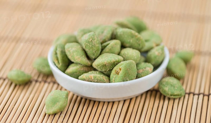 Wasabi coated Peanuts as high detailed close-up shot on a vintage wooden table (selective focus)