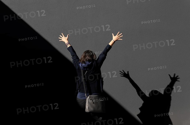Woman Standing with Arms Raised Against a Grey Wall with Diagonal Shadow in a Sunny Day in Switzerland