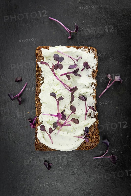 Slate slab with cream cheese and fresh cress on a slice of wholemeal bread (close-up shot, selective focus)