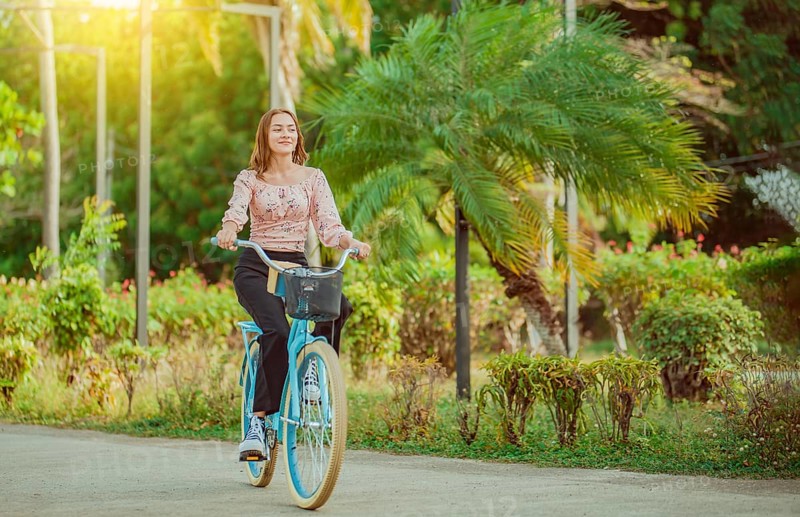 Beautiful and smiling young woman riding a bicycle in a nice park, looking at camera. Cheerful Latin girl riding a bicycle in a green park
