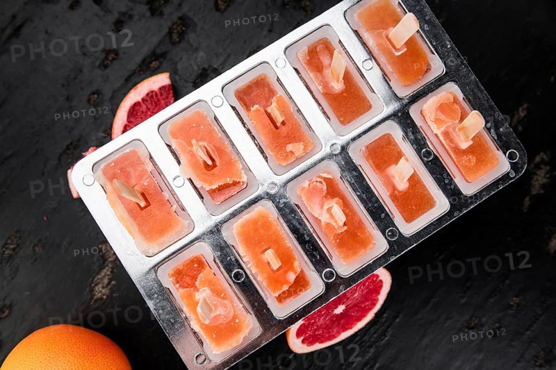 Some homemade Grapefruit Popsicles (with some fresh fruits) as close-up shot (selective focus)