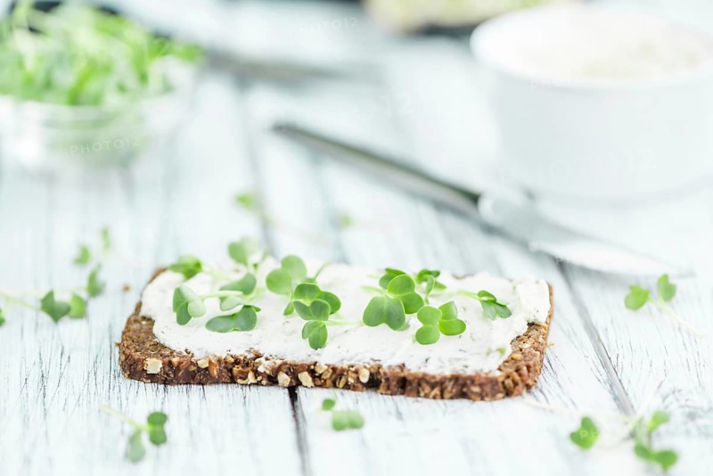 Slice of wholemeal bread with fresh cutted cress and cream cheese on an old wooden table (selective focus, close-up shot)