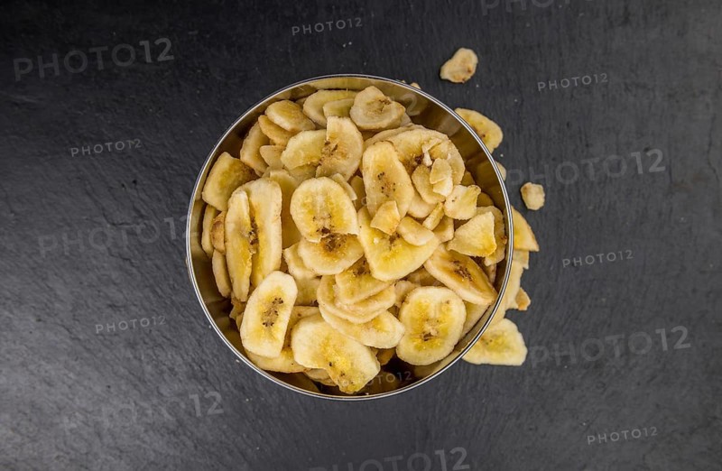 Some Dried Banana Chips on a slate slab as detailed close-up shot, selective focus