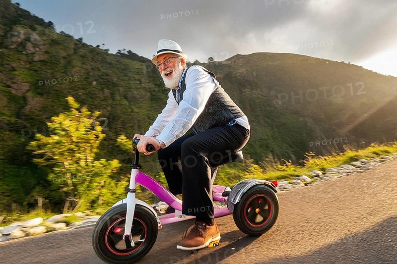 An elderly man rides a tricycle on a road in the middle of a natural environment and laughs happily, AI generated, AI generated