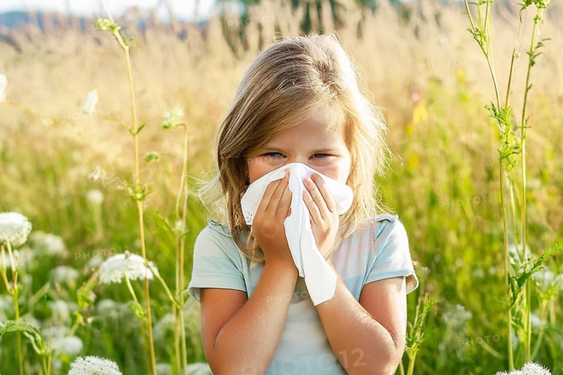 A little girl stands in a meadow of flowers and blows her nose with a handkerchief, surrounded by golden sunlight, AI generated, AI generated
