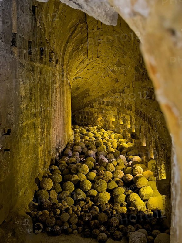 Historical vaulted corridor today illuminated with yellow light inside old stone bullets stones cannonballs historical ammunition in fortress built in the Middle Ages 16th century by Republic of Venice old name Castello Rocca al Mare today Koules in harbour of Iraklion today museum, Heraklion, Crete, Greece, Europe