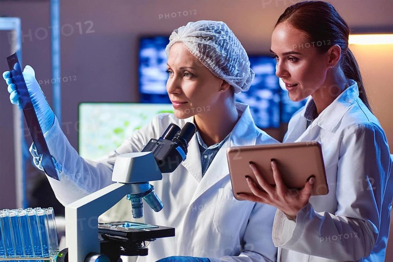 Two lab assistants analyse samples, one at the microscope, the other with a tablet, AI and illustration technology, AI generated