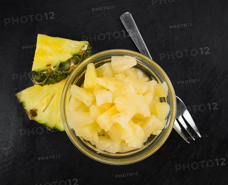 Portion of Preserved Pineapple (chopped) as detailed close up shot on a slate slab, selective focus