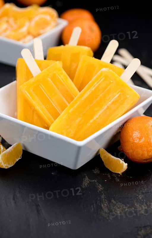 Portion of fresh homemade Tangerine Popsicles (close-up shot, selective focus) on a vintage background