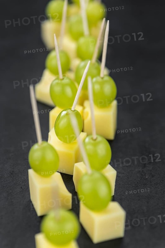 Cheese blocks with grapes as close-up shot on a vintage looking slate slab (selective focus, partyfood)