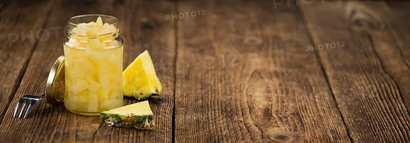 Chopped Pineapple (preserved) as high detailed close-up shot on a vintage wooden table, selective focus