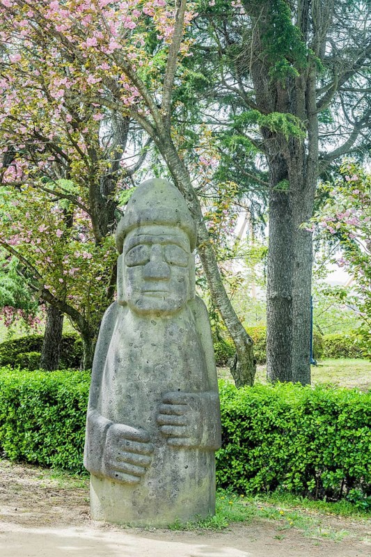 A large stone statue in a garden area with trees and bushes, in Suncheon, South Korea, Asia