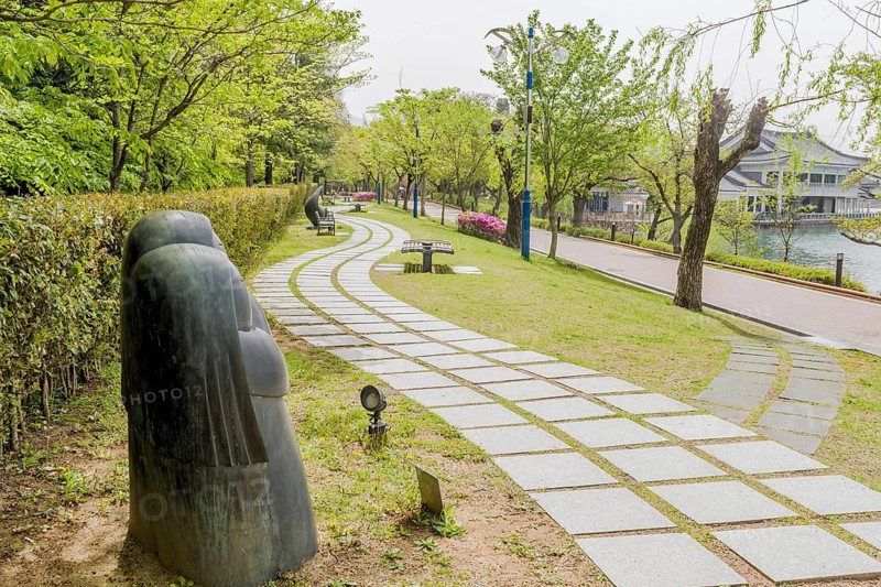Curved pathway lined with sculptures in a serene park filled with greenery and trees, in Suncheon, South Korea, Asia