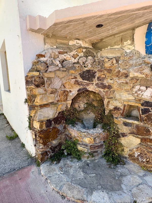Old well at the corner of the house next to the historic small single-nave church Panagia Throniotissa Naos Panagia of the Dormition of the Virgin Mary of the Assumption in Thronos built in the 14th century on part of the site of the destroyed predecessor church, the Episcopal Basilica of Sybrita, Thronos, Crete, Greece, Europe