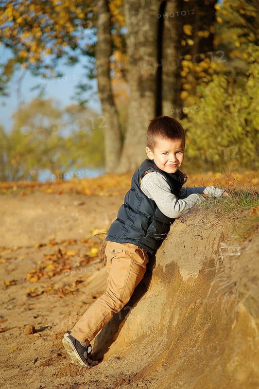 A young boy smiling and climbing a dirt slope in an autumn forest setting with colorful fall leaves, Belarus.Minsk