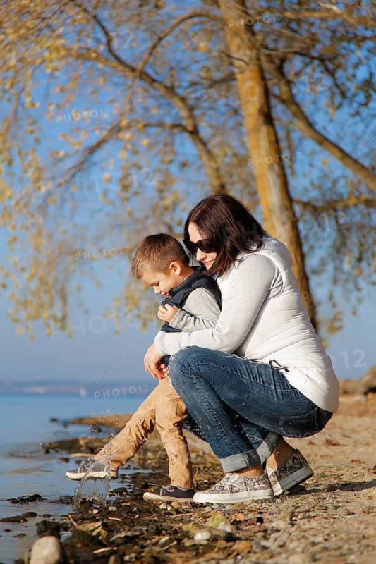 A woman and a child are kneeling by a lakeshore in autumn, enjoying the nature and calm atmosphere, Belarus.Minsk