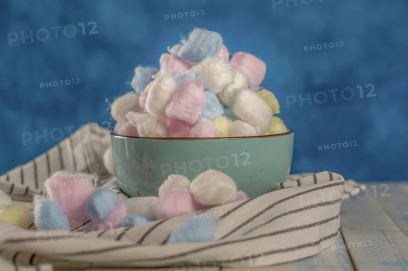 Cotton balls of different colors in a ceramic bowl on a blue background