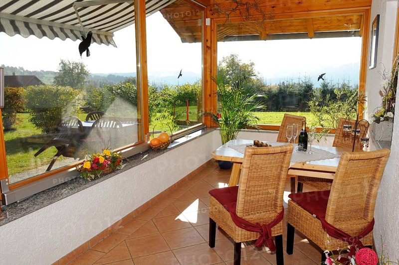 Cosy conservatory as a dining area with wooden table and chairs, surrounded by windows with views of the countryside, Bavarian Forest