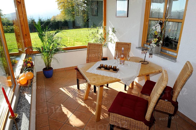 Cosy conservatory as a dining area with wooden table and chairs, surrounded by windows with views of the countryside, Bavarian Forest