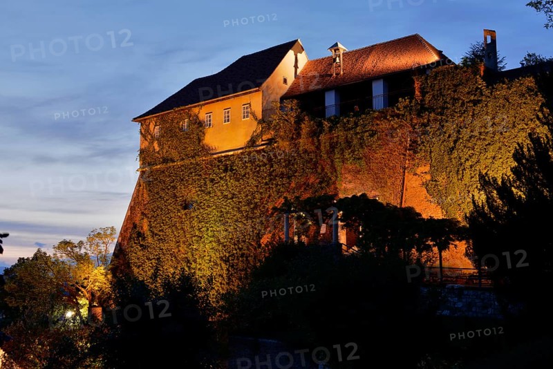 An illuminated castle at dusk with ivy-covered walls on a hill, Stallbastei, Schlossberg, Graz