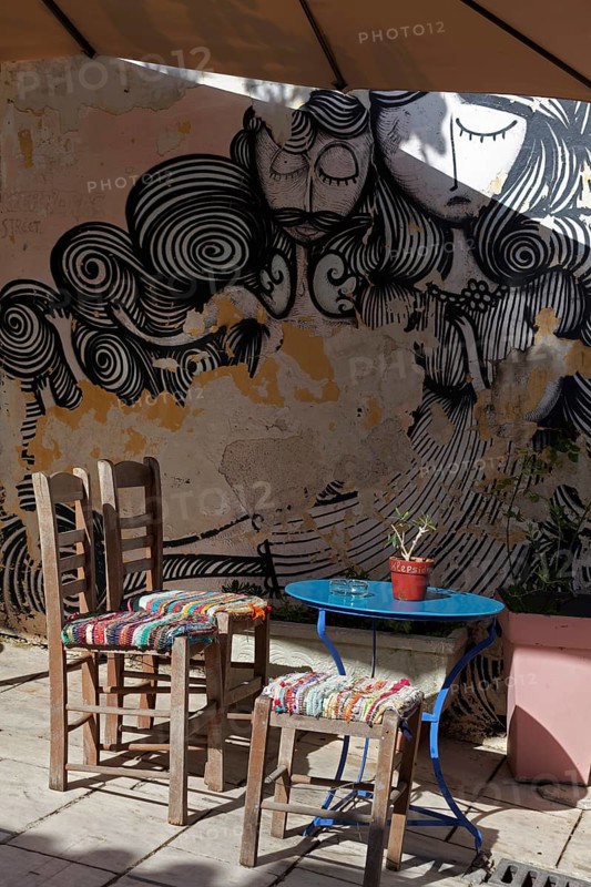Chairs and table in front of a wall with graffiti, taverna in the old town district of Plaka, Athens, Greece, Europe