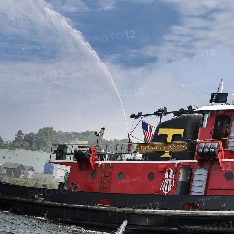 New London, Connecticut, USA, July 2012: The tug boat Patricia Ann spews water and flies an American flag giving a fire fighting salute during the Parade of Sail for Operation Sail Connecticut 2012, celebrating the bicentennial of the War of 1812 and the penning of the Star Spangled Banner, the US National Anthem. The bright red Patricia Ann with a big yellow letter T is owned by the Thames Tug Boat Co. of New London, CT, North America
