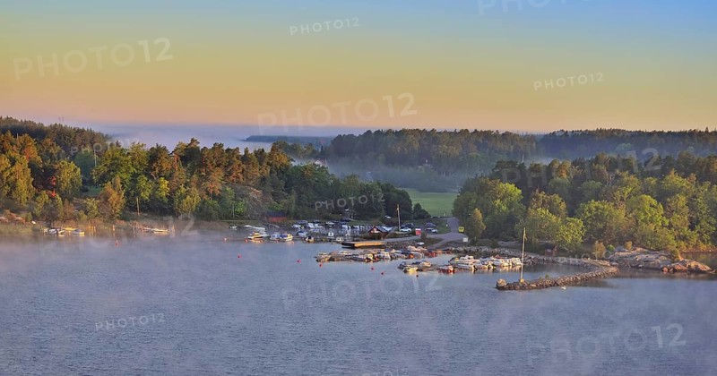 Sweeping panoramic view of boats moored amid the islands of the Stockholm Archipelago at dawn on a foggy morning seen from the Baltic Sea with stone pier swans and cygnets, Sweden, Europe