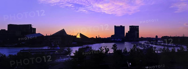 A dramatic and beautiful panoramic sunrise with buildings and boats in silhouette reflected in the waters of Baltimore's Inner Harbor Harbour Maryland, USA. Skyline includes the tall ship Chesapeake (far left) National Aquarium in Baltimore (triangular building and attached), Legg Mason building (tall building on right)