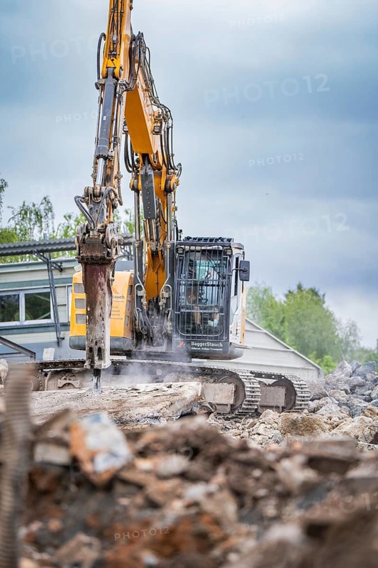 Excavator breaking up concrete on a building site. Debris and dust are scattered around the excavator, the sky is cloudy, demolition site, Saarbrücken, Germany, Europe