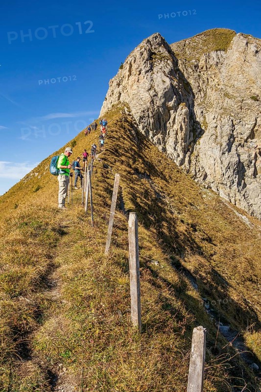 People hiking on a narrow mountain path with a steep ascent and rocky cliffs on a sunny day, saas Fee, Alps, Switzerland, Europe