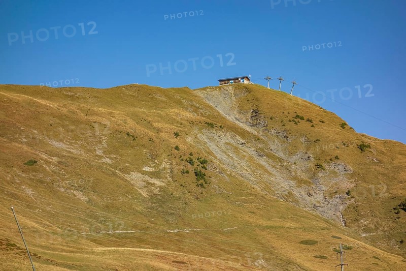 Extensive mountain landscape with a hut on a hill, crossed by a cable car under a blue sky, Grisons, Switzerland, Europe