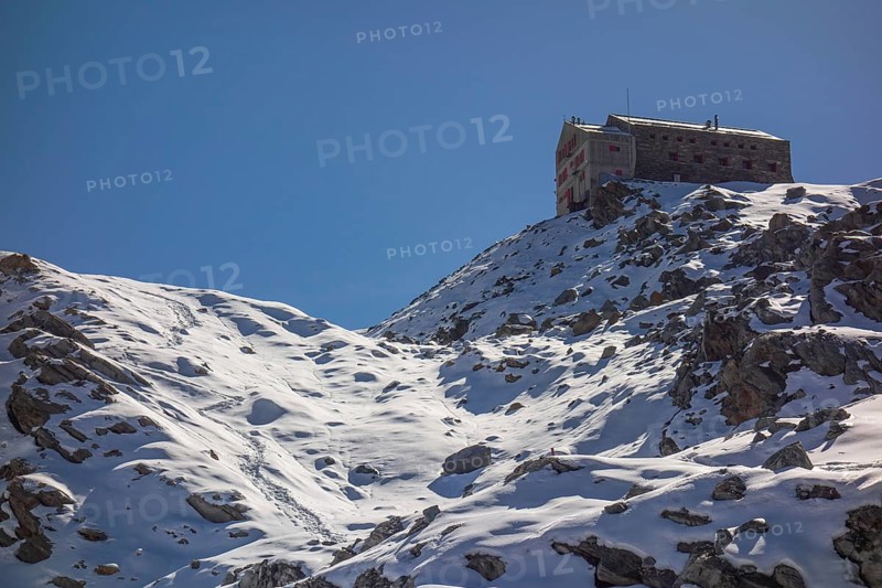 A lonely mountain hut perched on a snow-covered rock, surrounded by a wintry landscape with blue skies, saas fee, switzerland